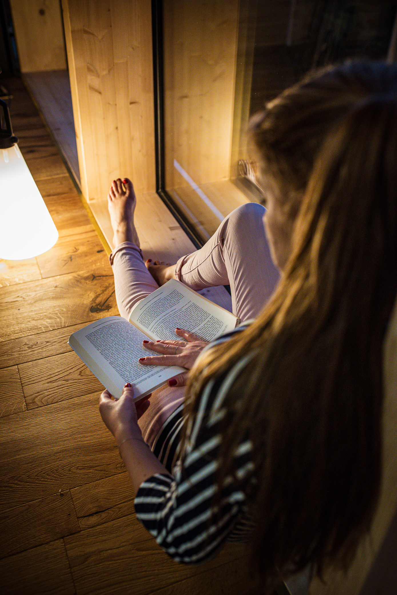 Jeune femmes en train de lire un livre, assises près d'une fenêtre. Elle est éclairé uniquement par une lampe